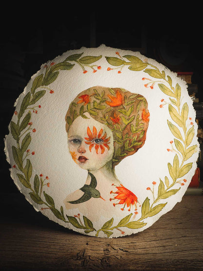 This original Idania Salcido (Danita Art) painting was made on a circular 12 x 12 Inch handmade watercolor paper, depicting a beautiful woman representing mother nature, with a wreath around it, orange flowers in her hair, a flower around her eye and a flying green bird at her shoulder.