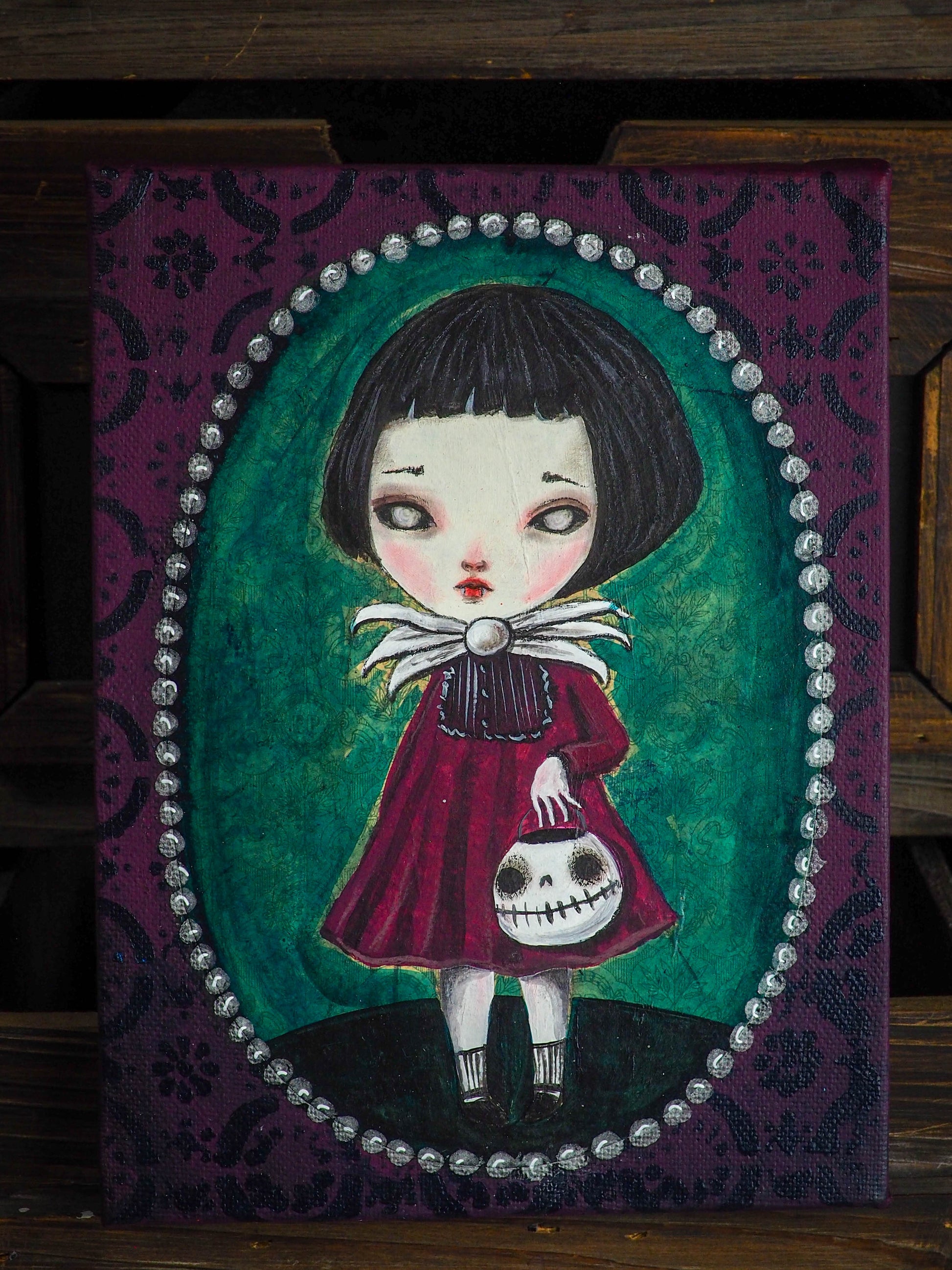 Original painting by Danita, a vampire undead zombie ghoul girl with Halloween with a skull pumpkin jack-o-lantern in her arms. Whimsical and surreal art perfect as home decor this Halloween Night.